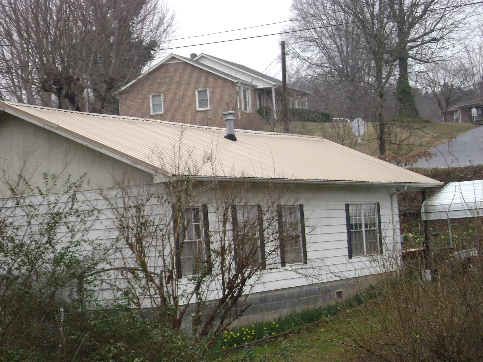 Tan metal roof on a white sided house set into a hillside — Commercial Roofing by Roofing Brothers in Sun Valley